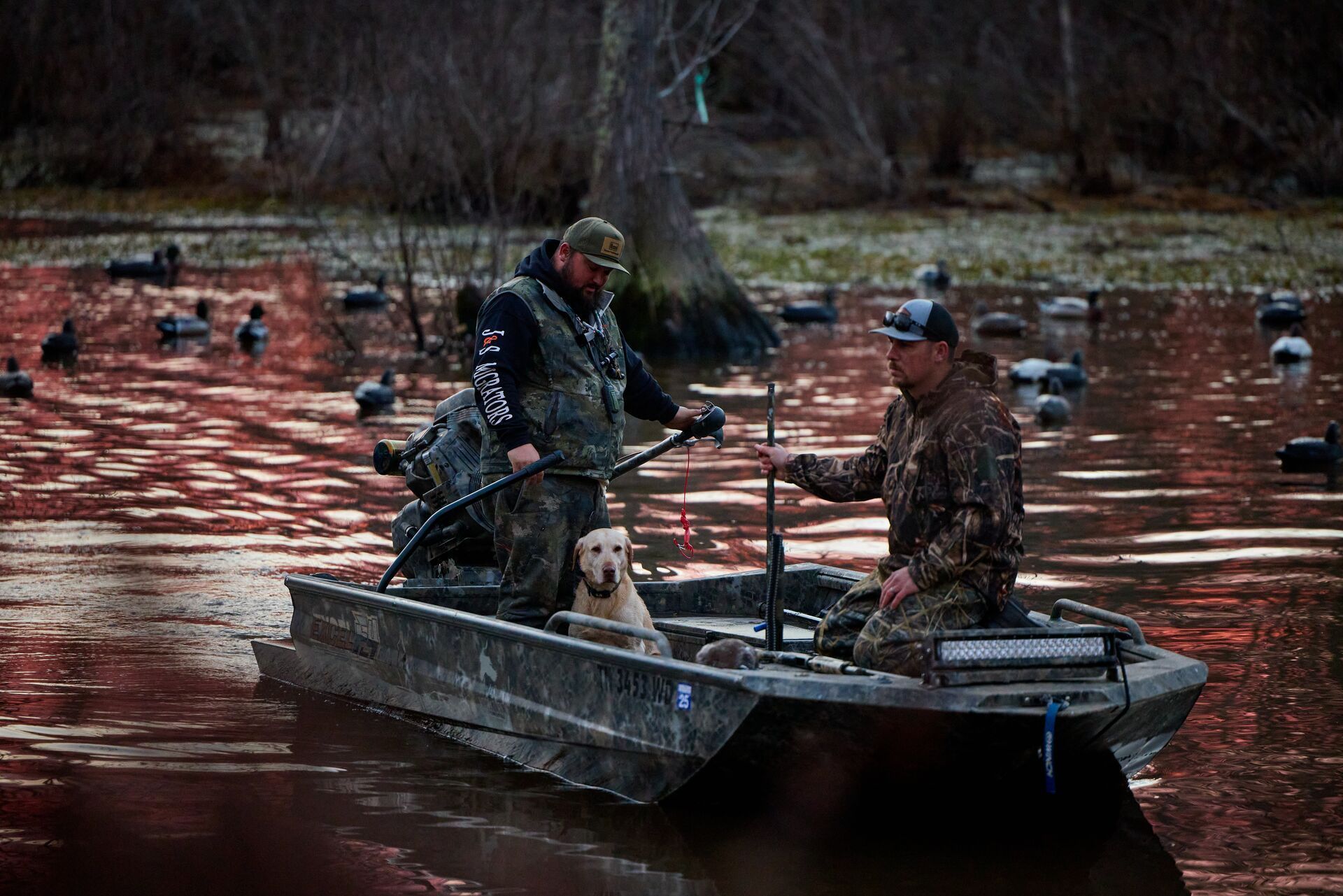 Two hunters in a boat with a dog to hunt waterfowl.