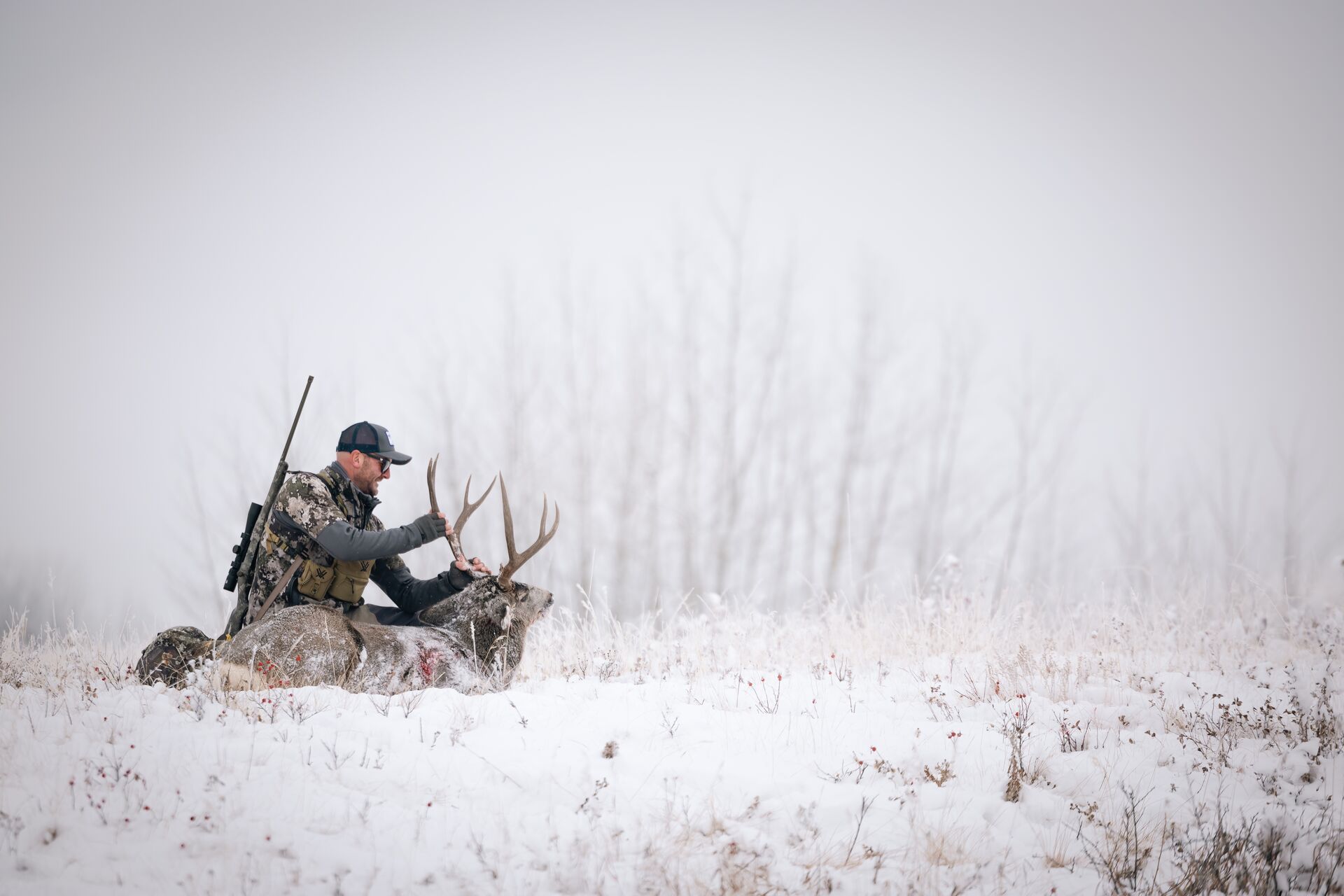 Hunter with rifle and deer on ground in snow, late-season whitetail deer hunting tips concept.