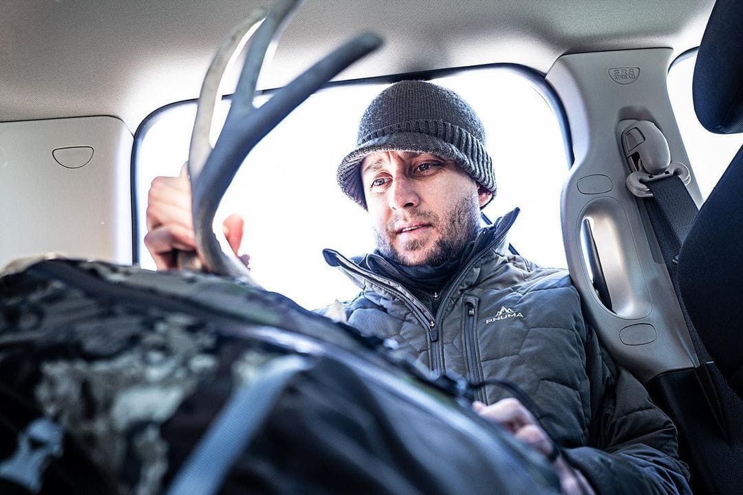 A hunter looks at deer antlers while in the back seat of a truck.