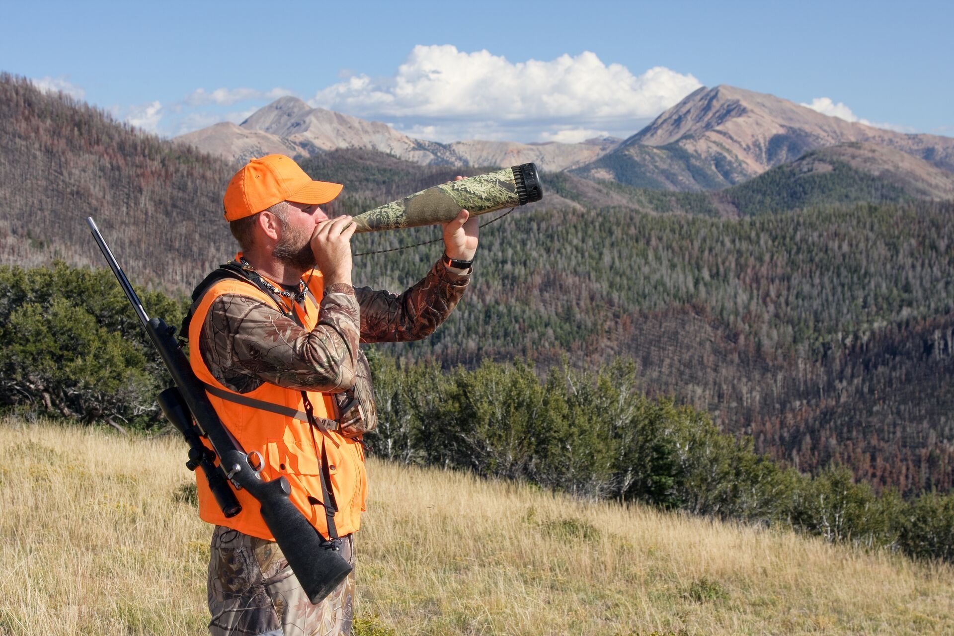 Hunter in blaze orange on hill using elk bugle call.