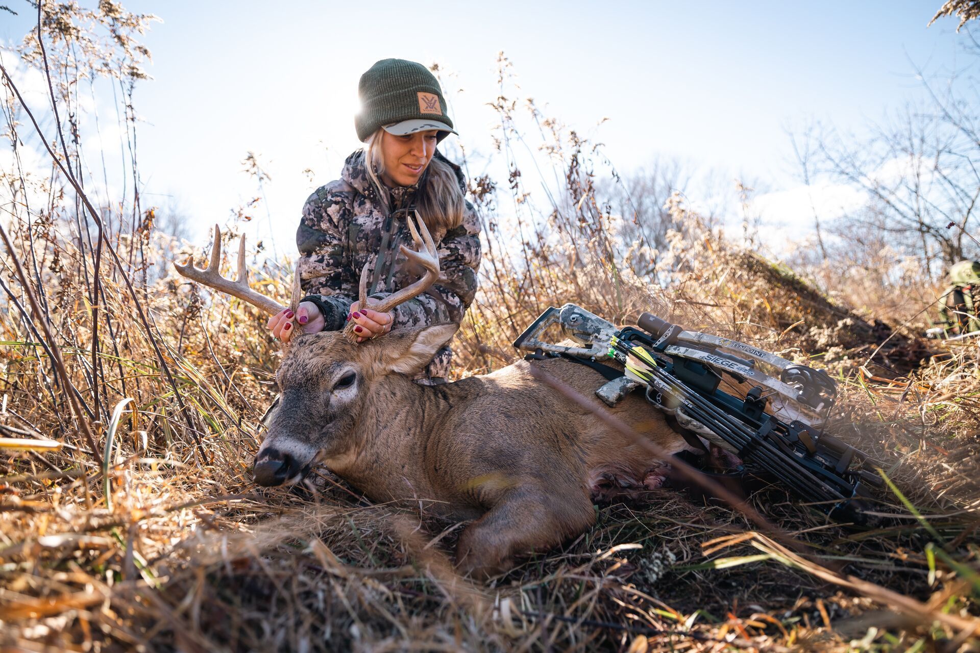 Female hunter with deer and bow on ground after hunt, Alabama deer season concept.