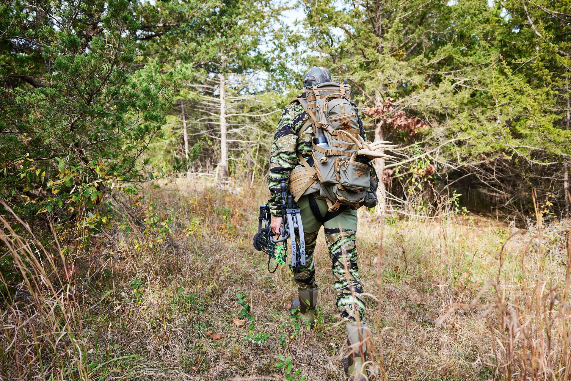 John Dudley walks into the woods with hunting gear, use the HuntWise hunting app concept.