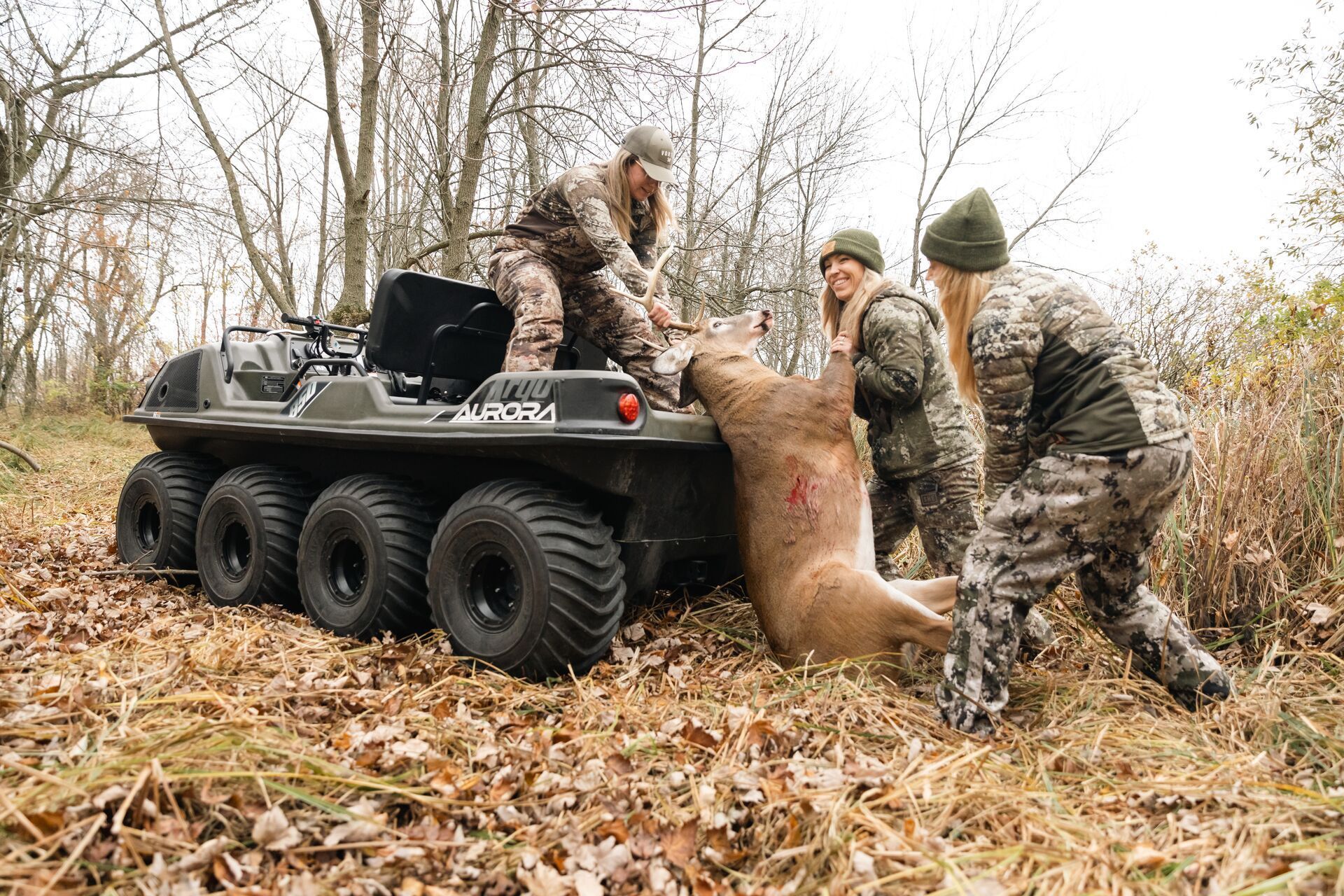 Three female hunters load a buck onto a tractor after a hunt.