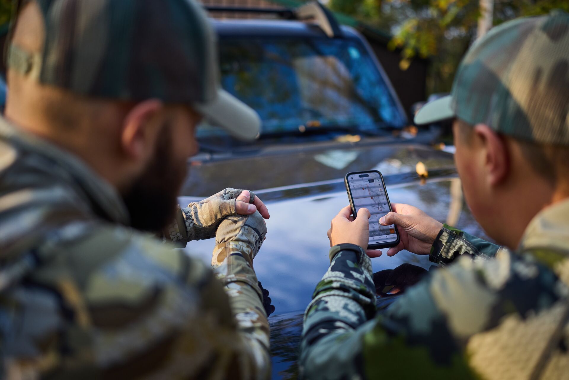 Two hunters look at phone showing HuntWise maps on screen.