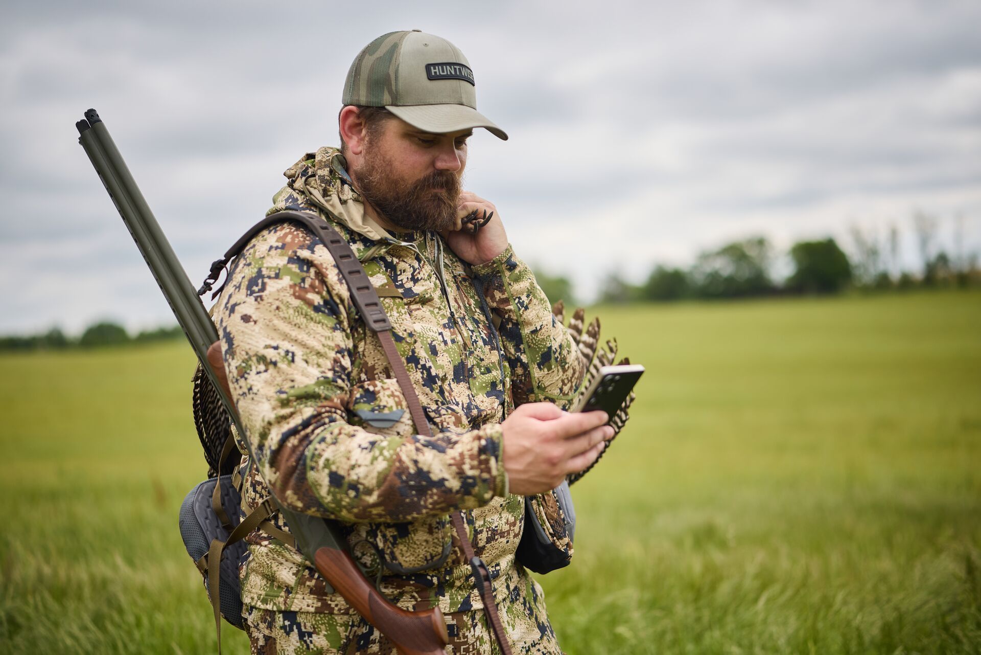 Hunter in camo in field using phone, find public hunting land with HuntWise.