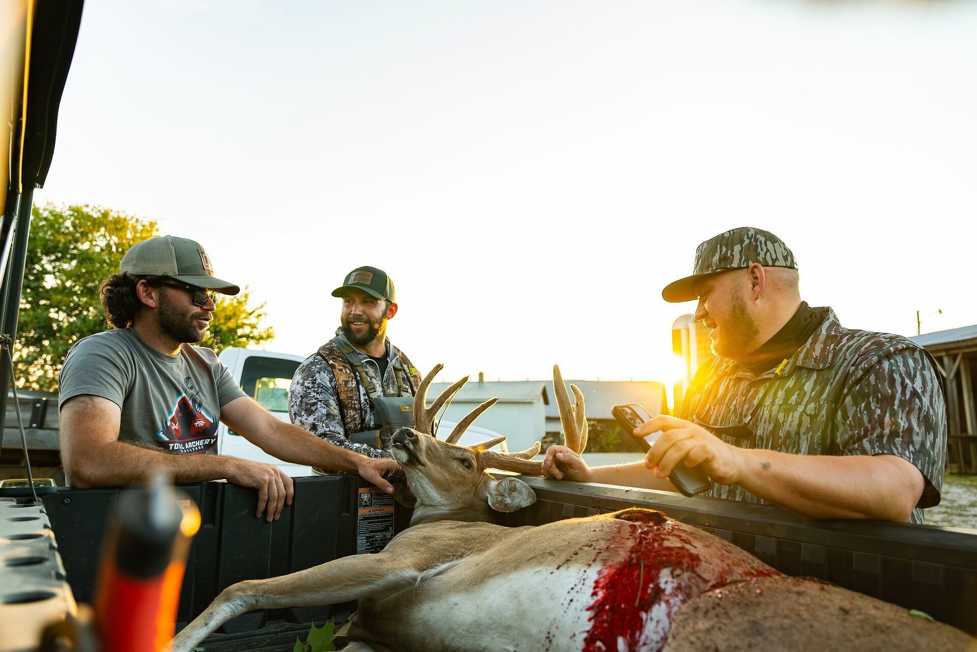 Three hunters with a buck deer in back of truck after hunt, pre-rut hunting whitetail concept.