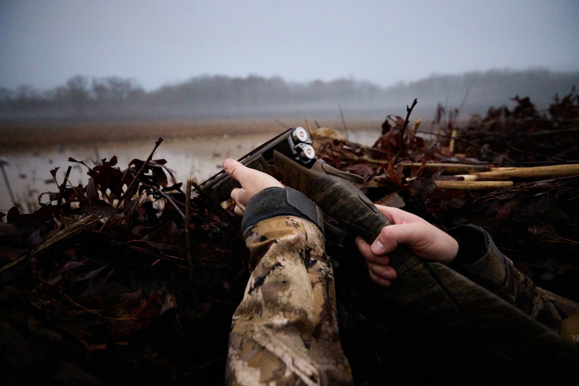 Hunter opens shotgun to reload while in duck blind, shotgun for hunting concept.