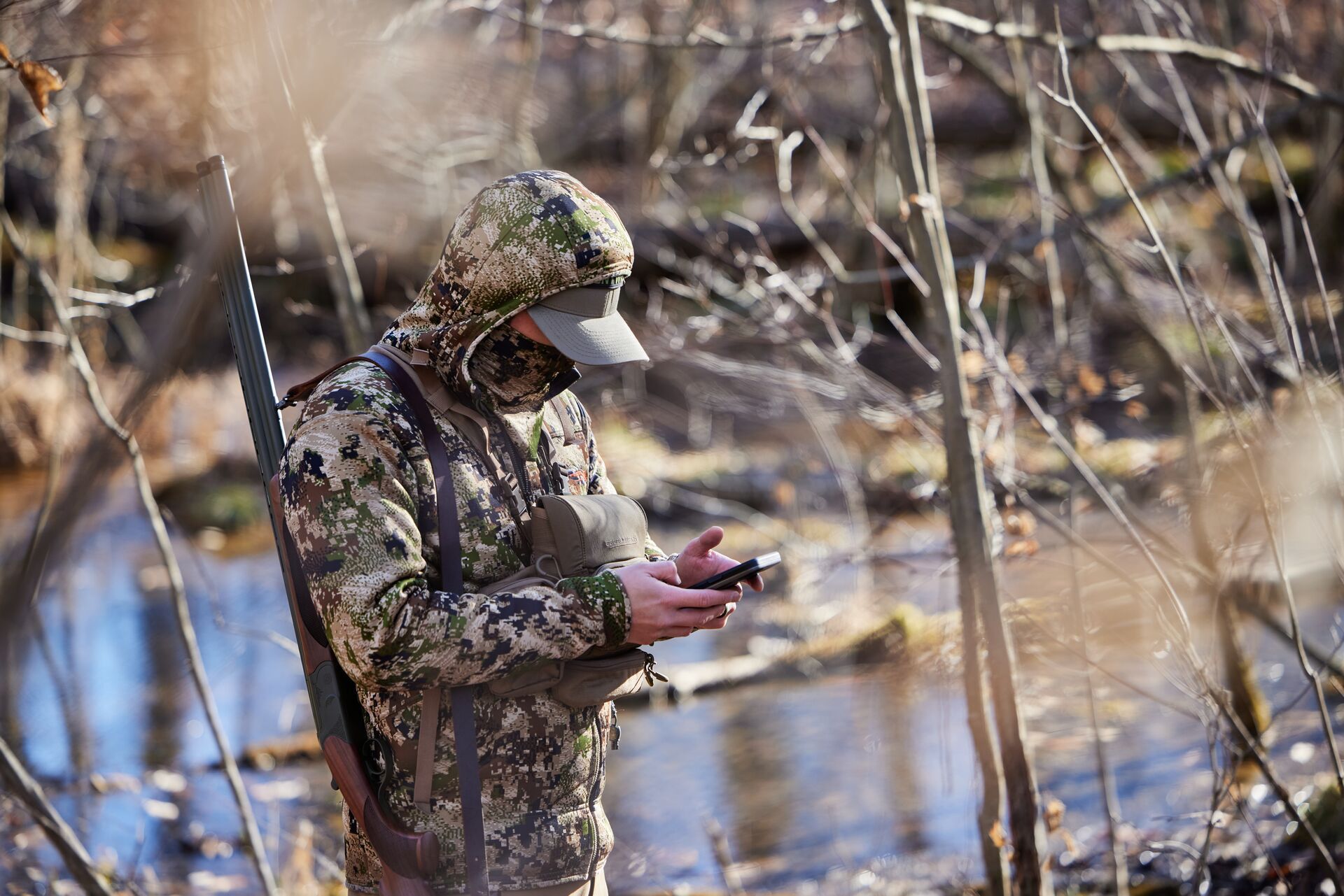 Hunter in turkey gear in field using phone for HuntWise, best turkey hunting weather concept.