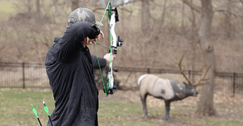 John Dudley at full draw aiming a compound bow at a target.