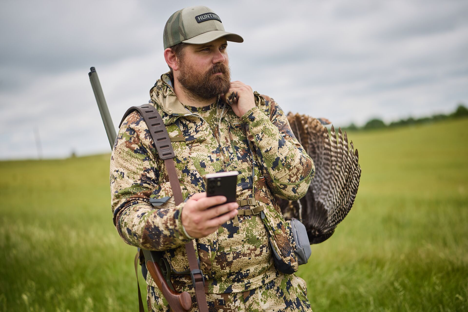Hunter in camo with turkey gear holding phone, how to use a hunting app to hunt public land.
