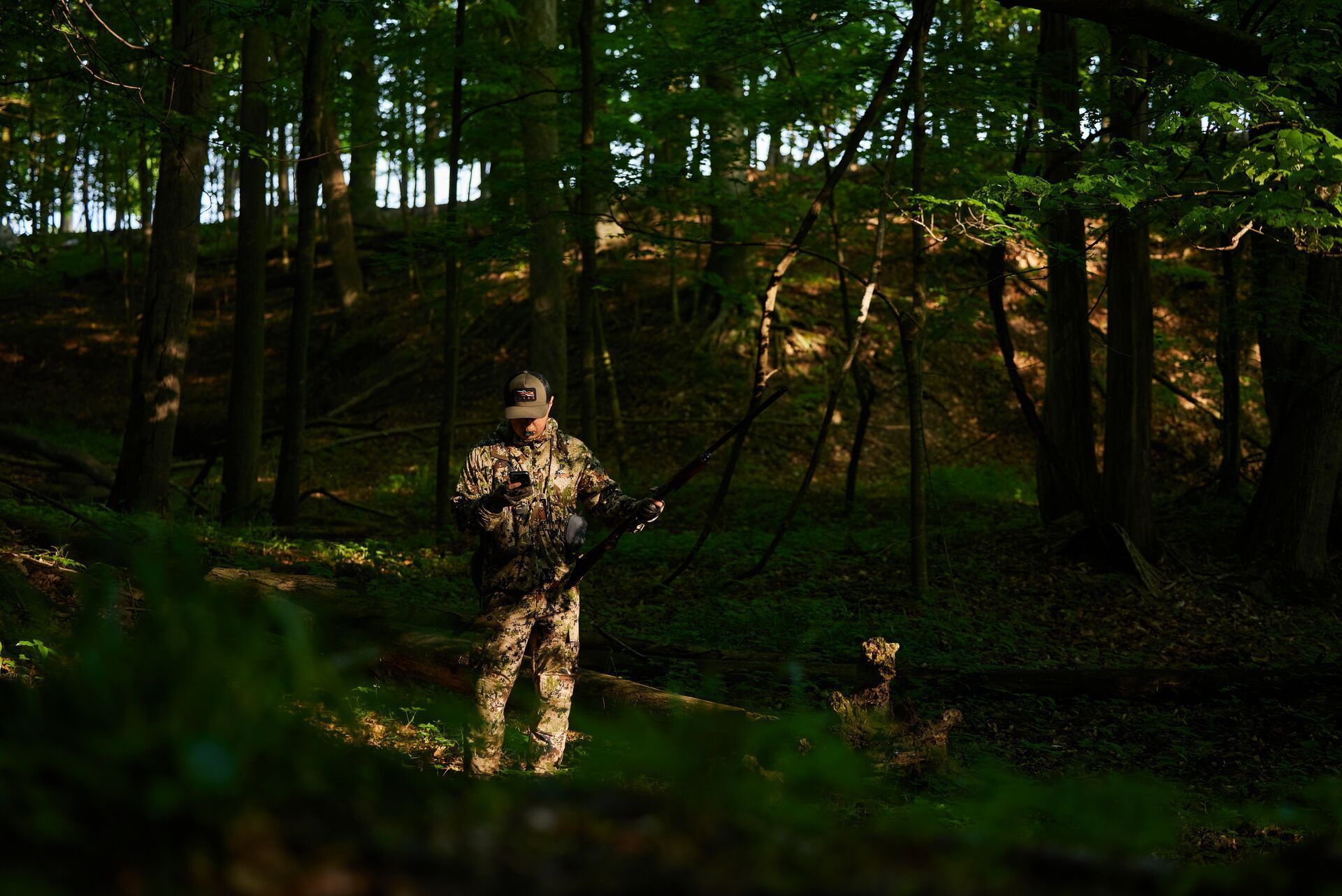 A hunter in the woods looking at a phone, using HuntWise for turkey season Minnesota concept.
