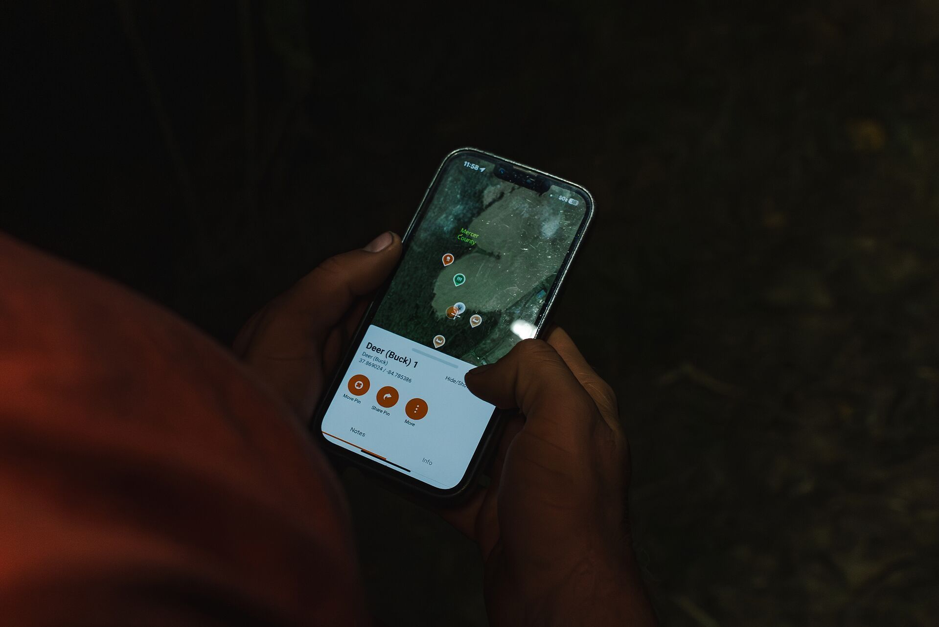 In the dark close-up of hands showing HuntWise on phone screen, Minnesota deer season.