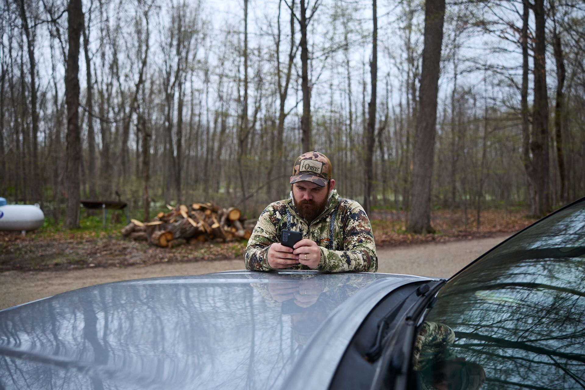 A hunter uses a hunting app on a phone while leaning on a truck.