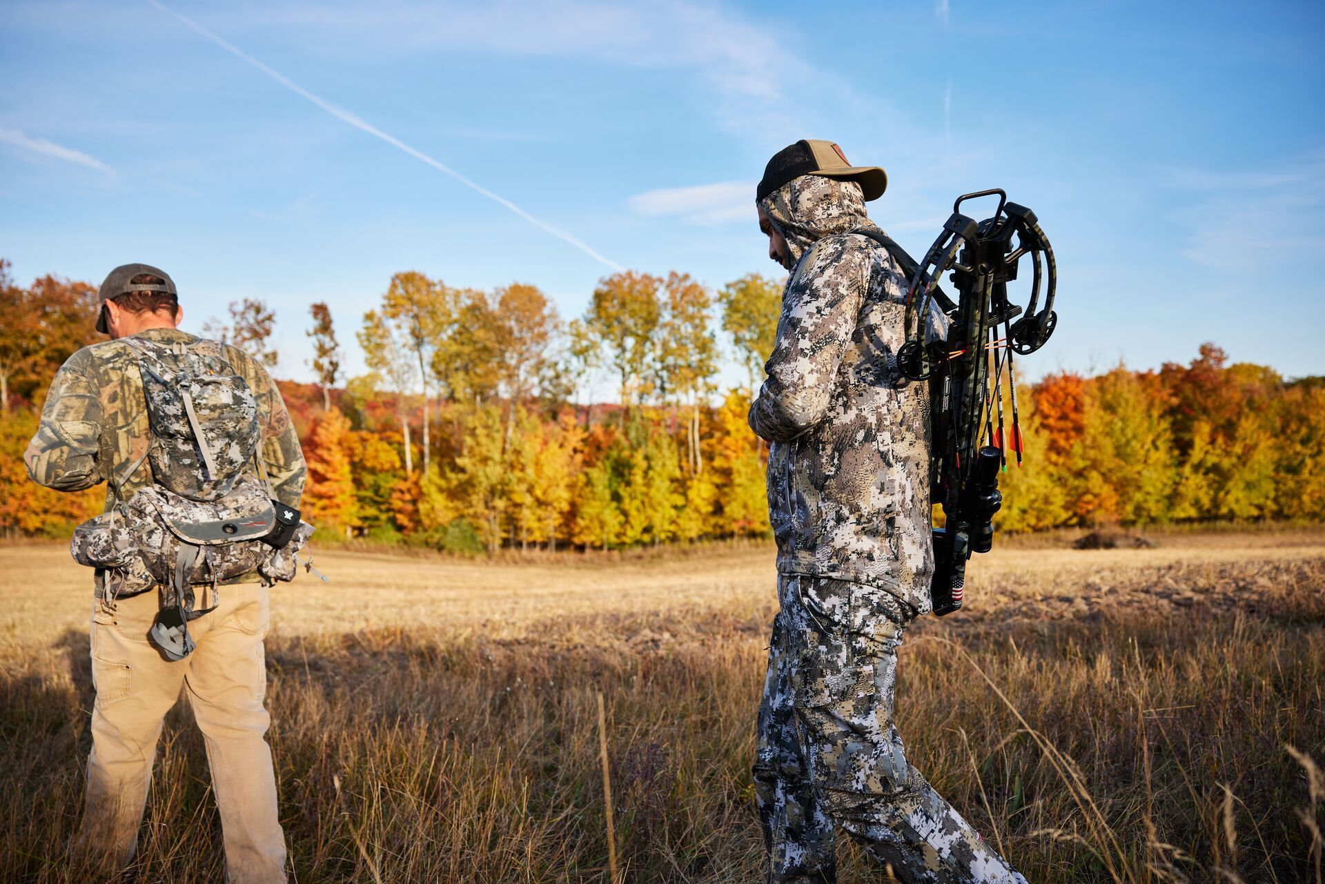 Two hunters in camo with gear walk across hunting land, know private land hunting laws concept.