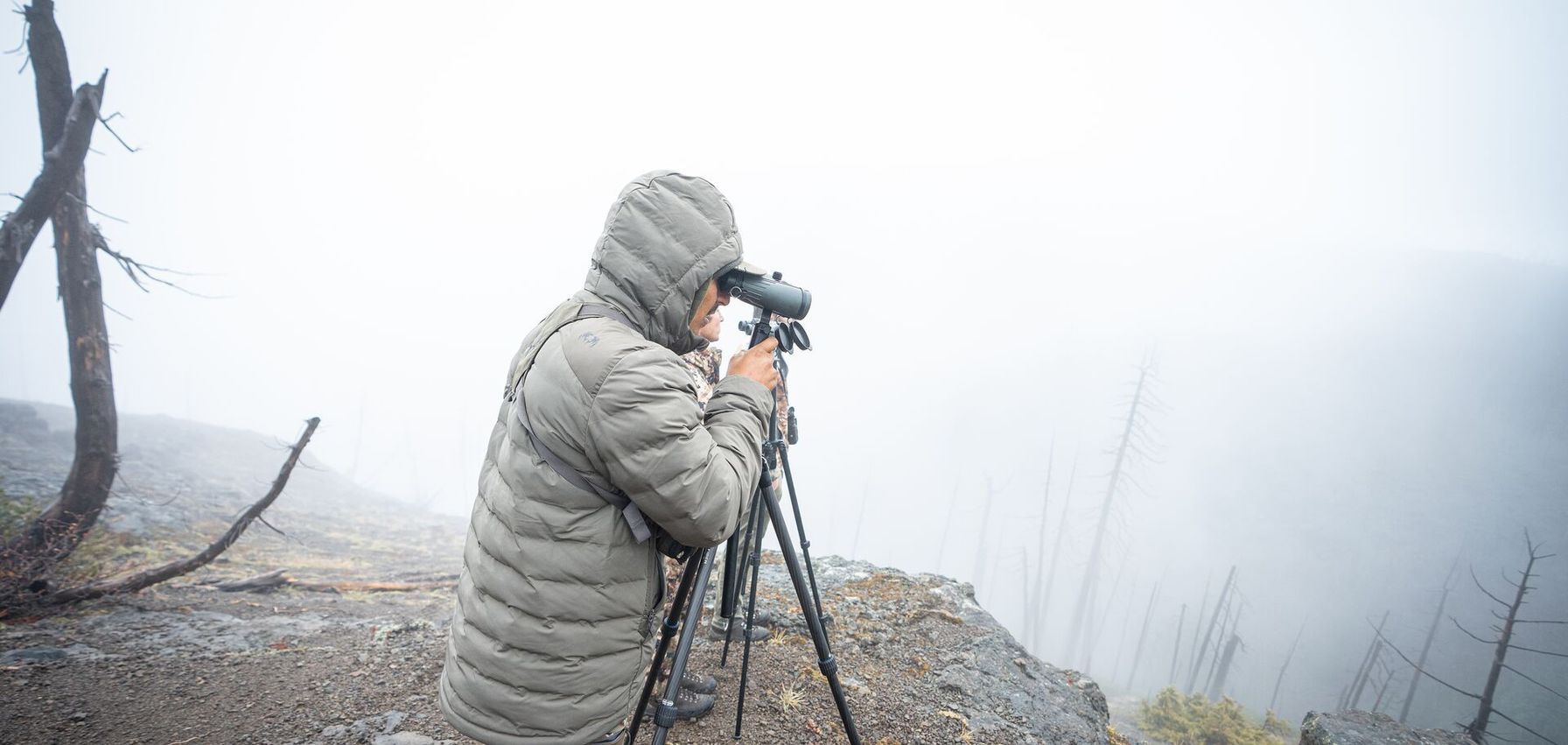 Hunter on an a ridge uses a spotting scope, when is mule deer season concept.