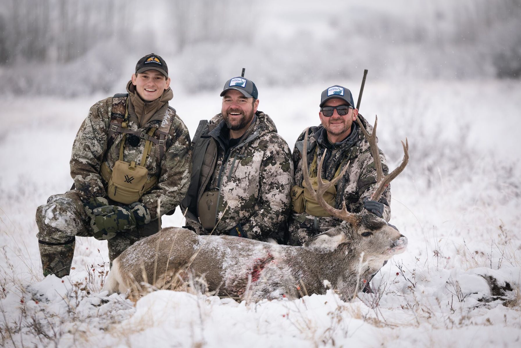 Three hunters post with buck deer after hunt.