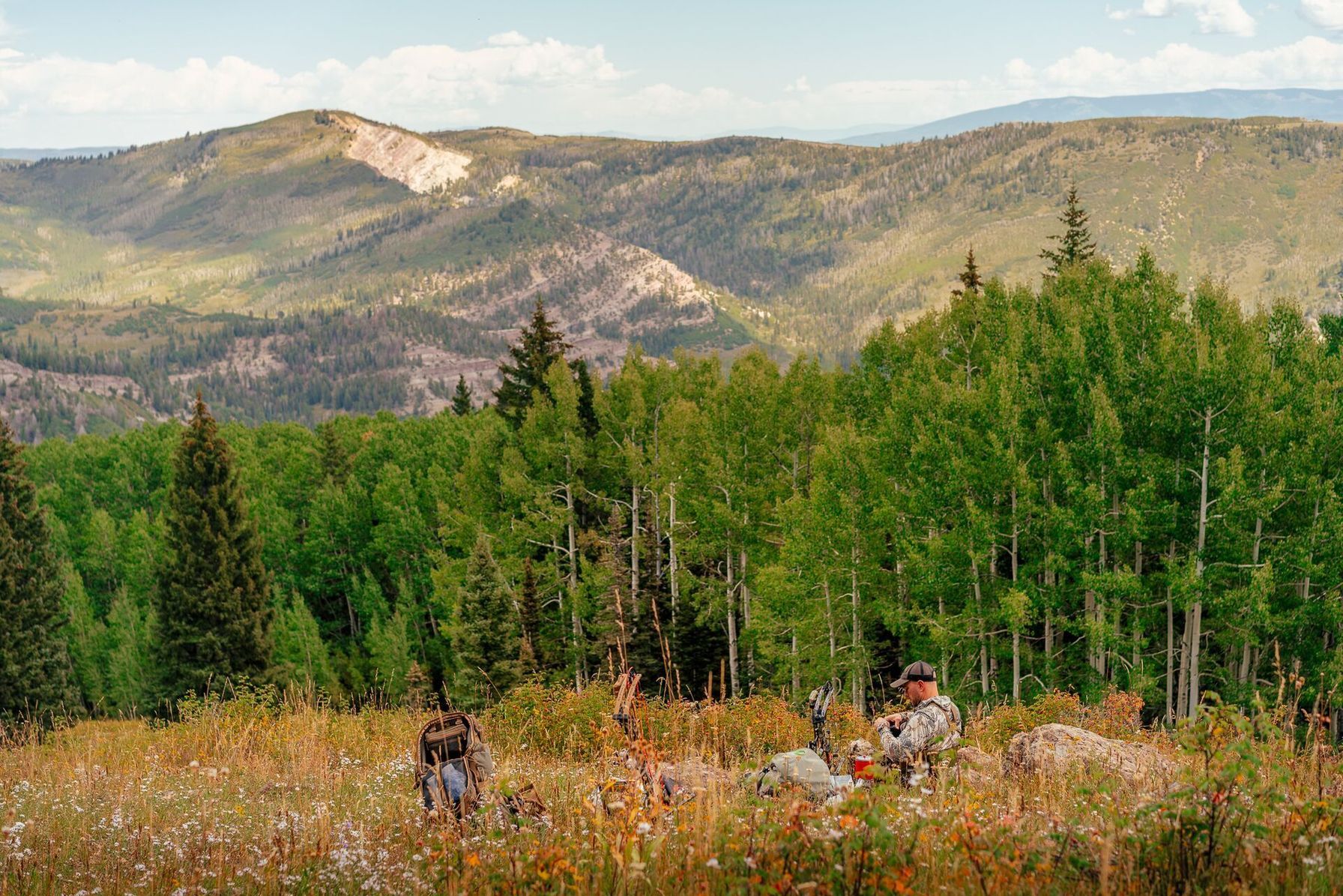 A hunter with gear sets up in a flowery field on a hill, what can you hunt in spring concept.