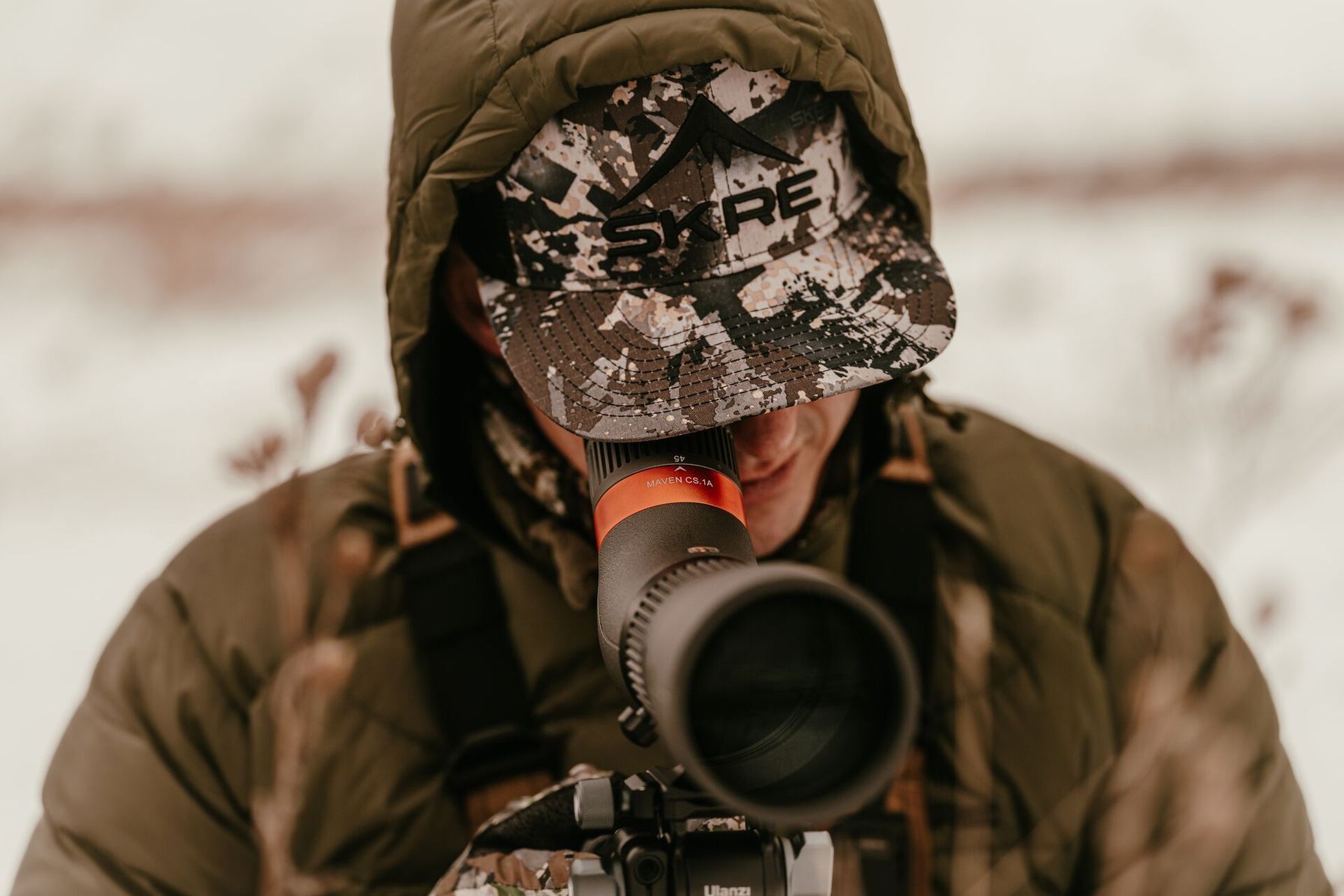 A hunter in a coat uses a scope for glassing, Montana hunting seasons concept.