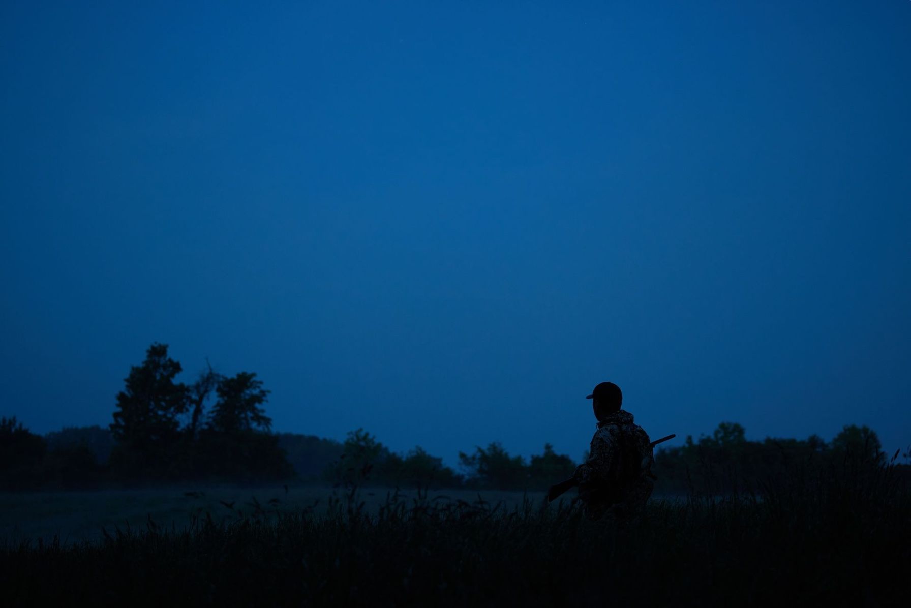 A hunter with a rifle in a field for night hunting.