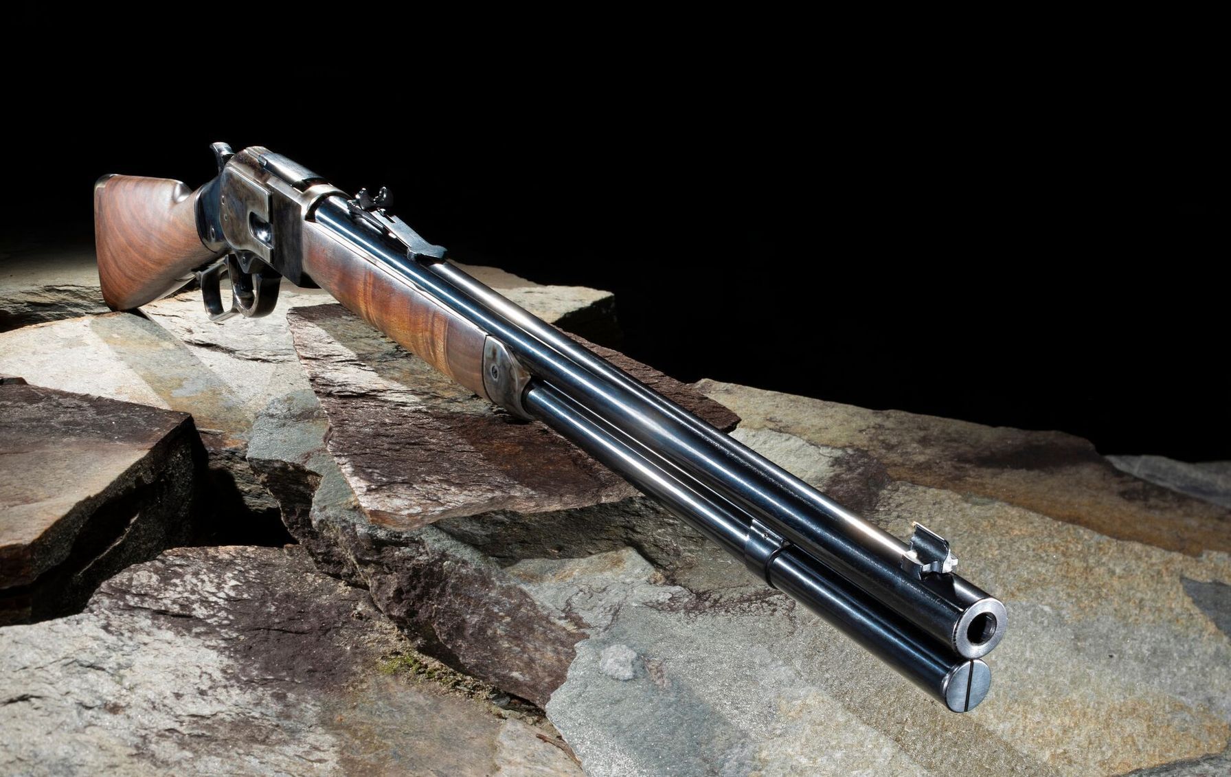 A lever action rifle sits on stone in front of a black background.