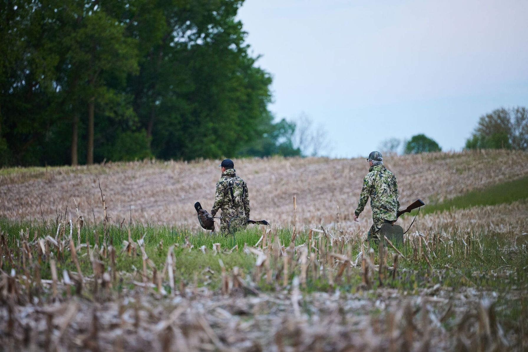 Two guys in camo on a turkey hunt in a field.
