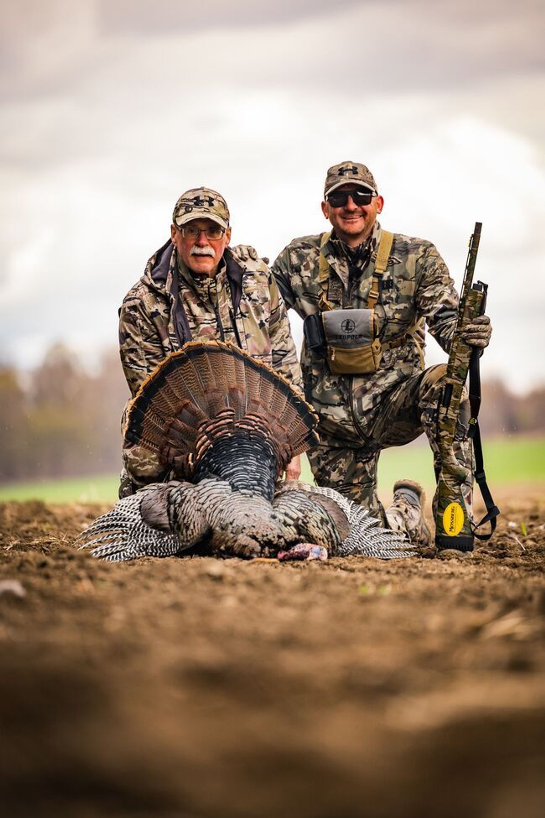 Two hunters smile and pose with turkey after hunt.
