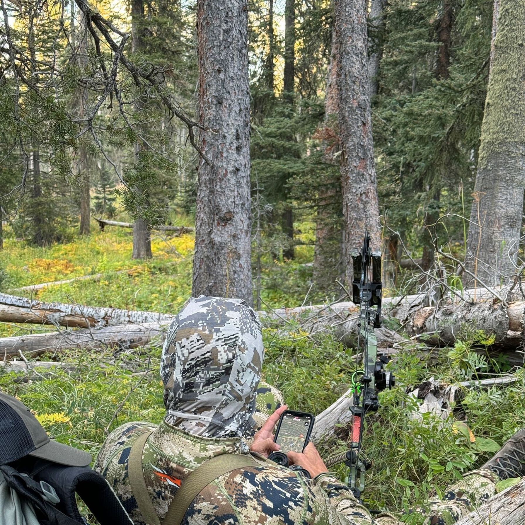Hunter with gear pack, clothing, bow, and HuntWise on phone..
