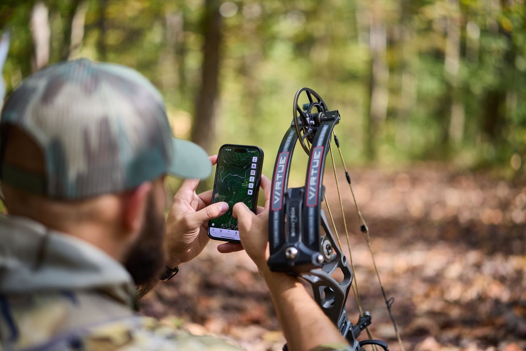 Hunter using the HuntWise app on phone with bow in woods.