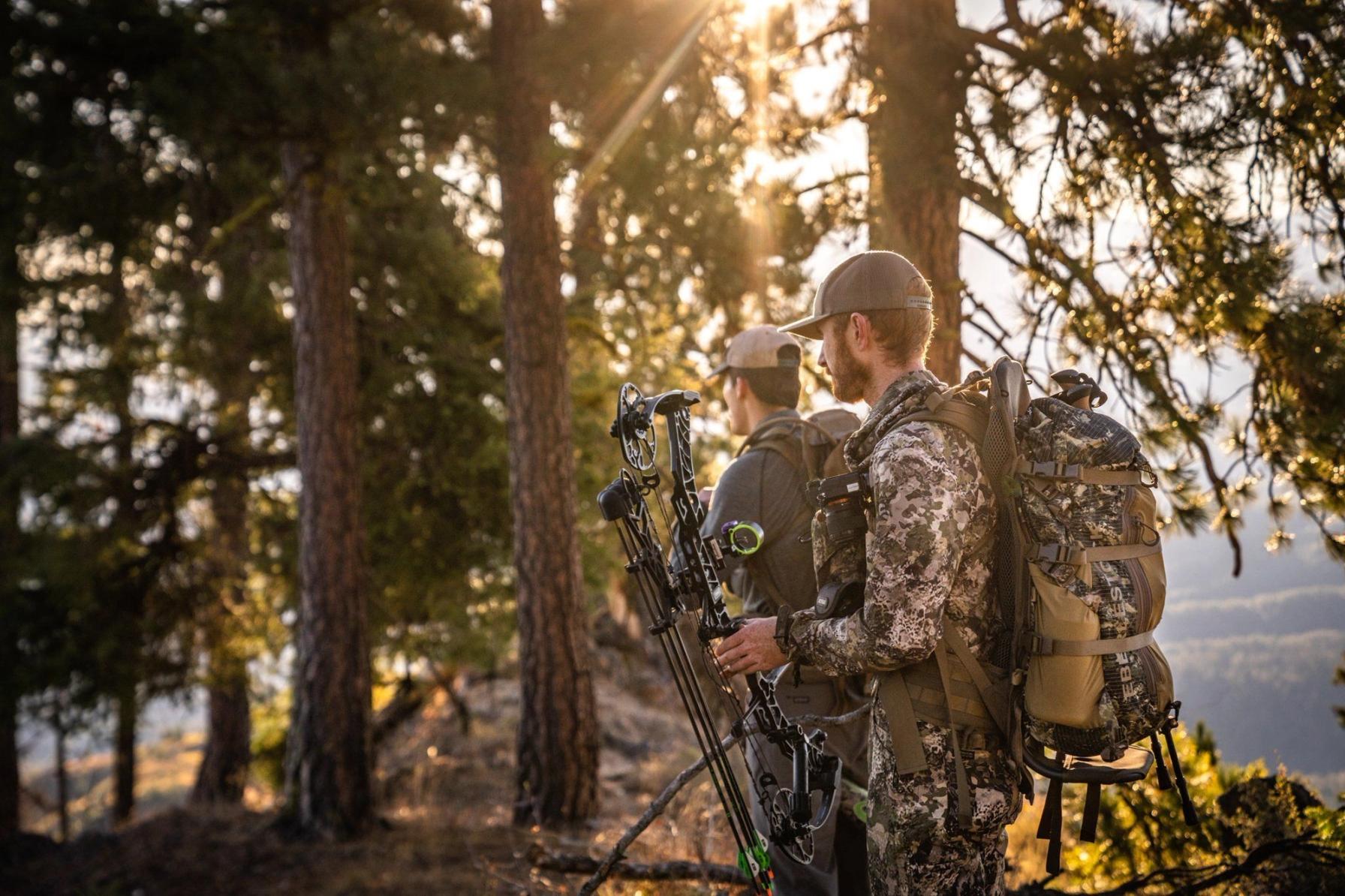 Two hunters in camo in the woods carrying bows, Mississippi hunting license concept.