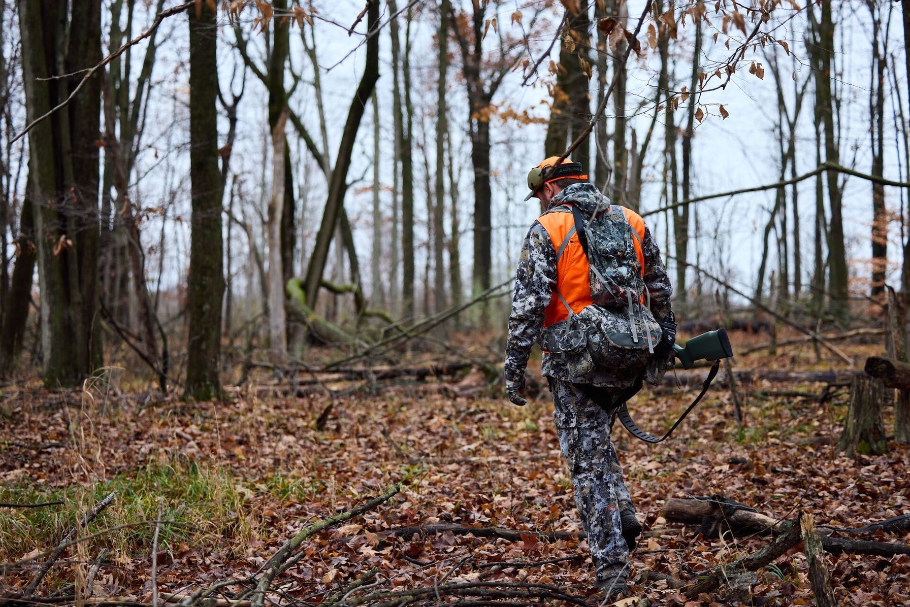 A deer hunter in the woods with a hunting rifle and gear.