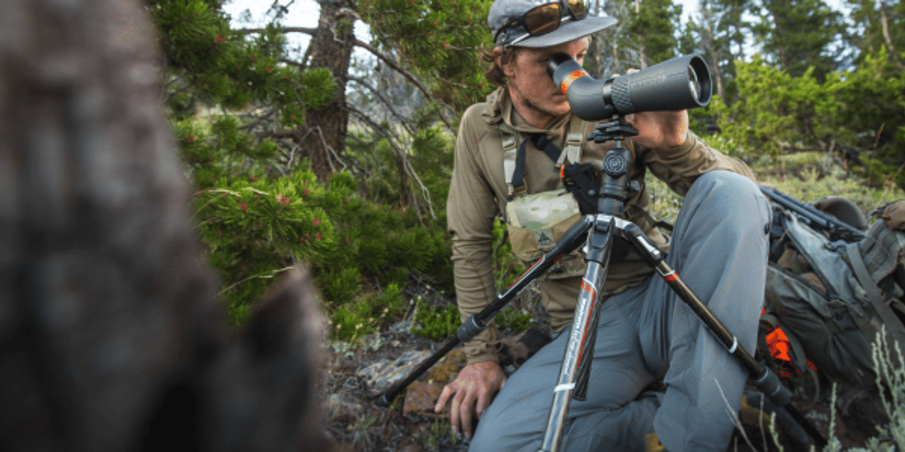 A hunter using a spotting scope on a tripod.