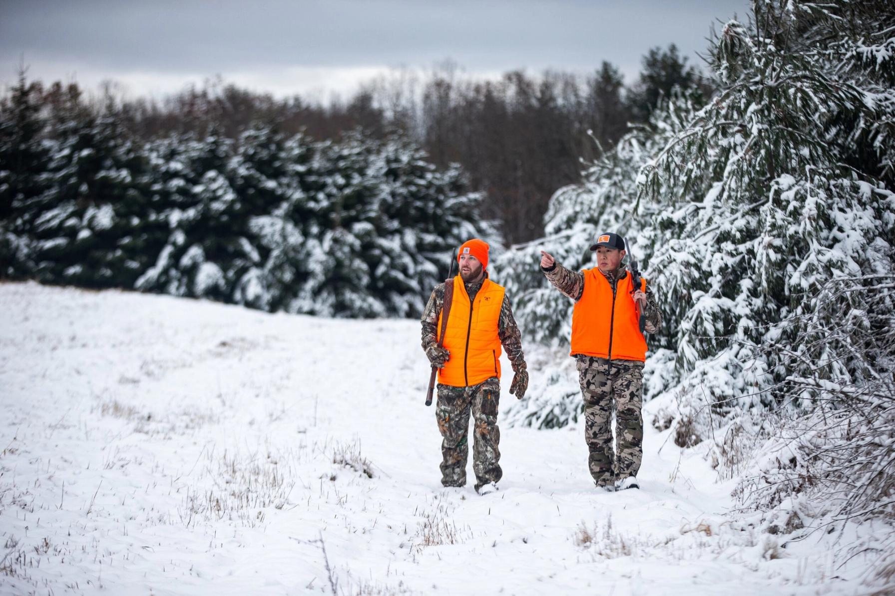 Two hunters in blaze orange and camo walk through snow for late-season hunting.