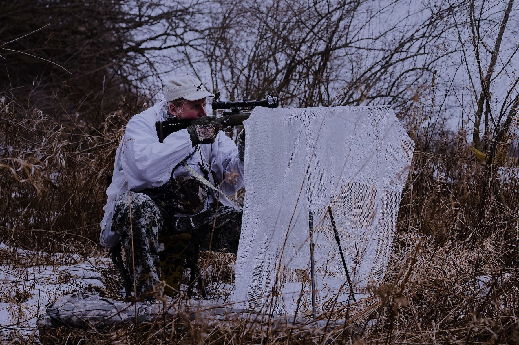A hunter with a rifle, scope, and gear for a coyote hunt at night.