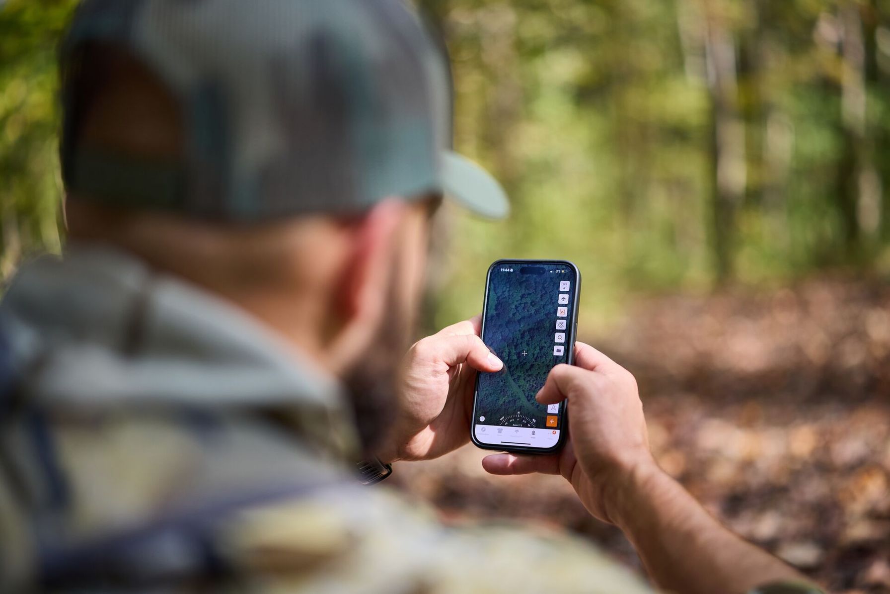 Hunter in the woods using HuntWise app on phone, rabbit trapping concept.