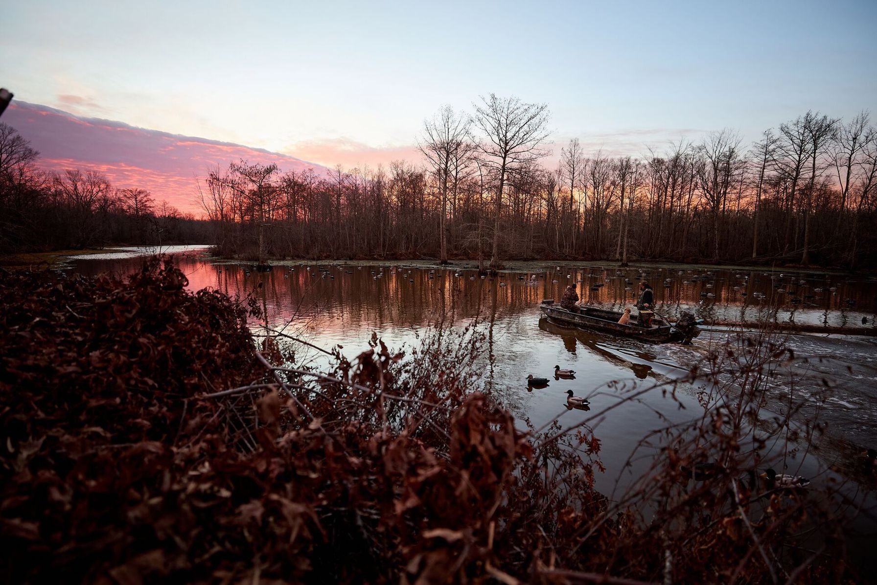 Wide shot of boat with hunters on water, use WindCast hunting app concept.
