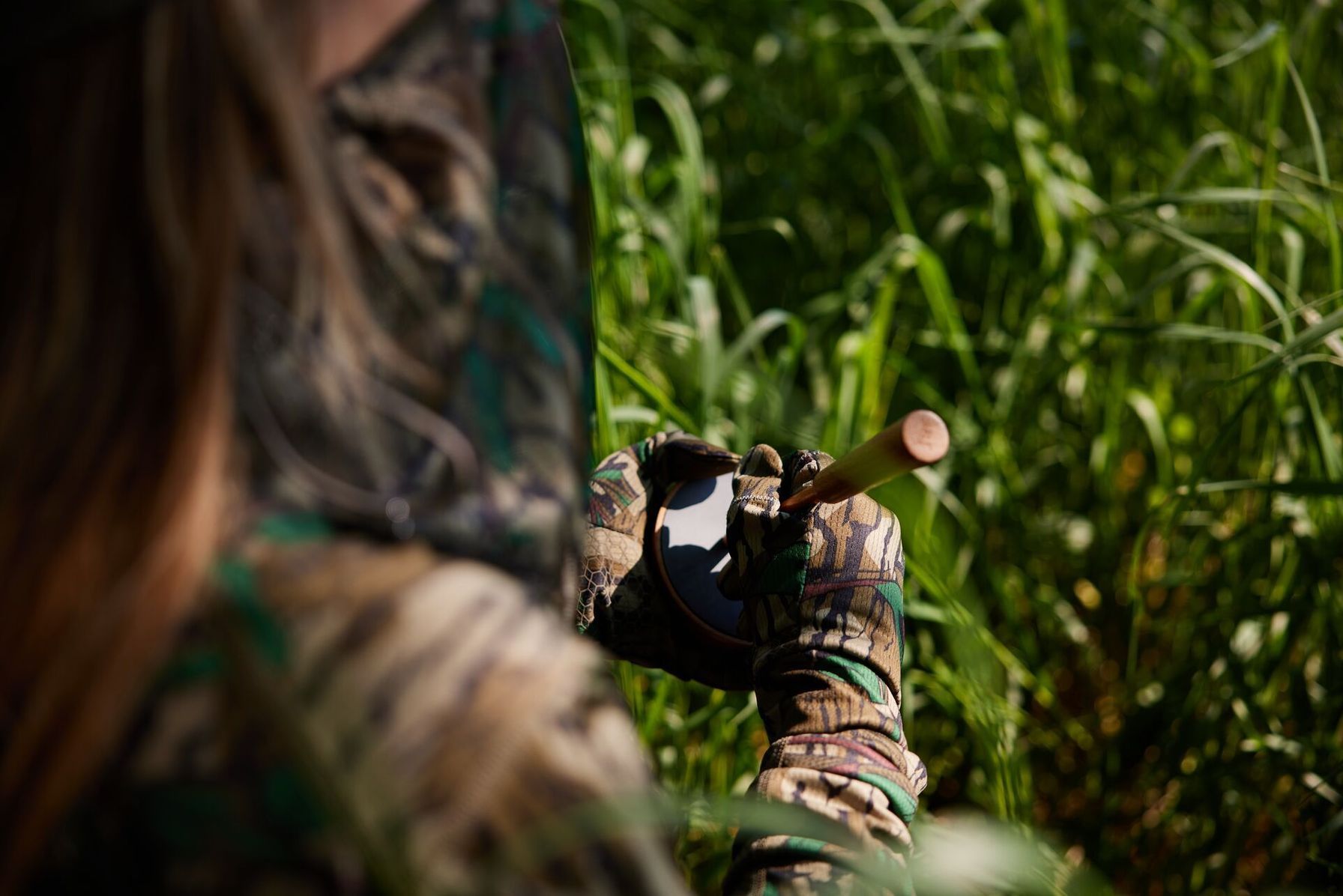 Close-up of a hunter using a turkey slate call while sitting in the brush.