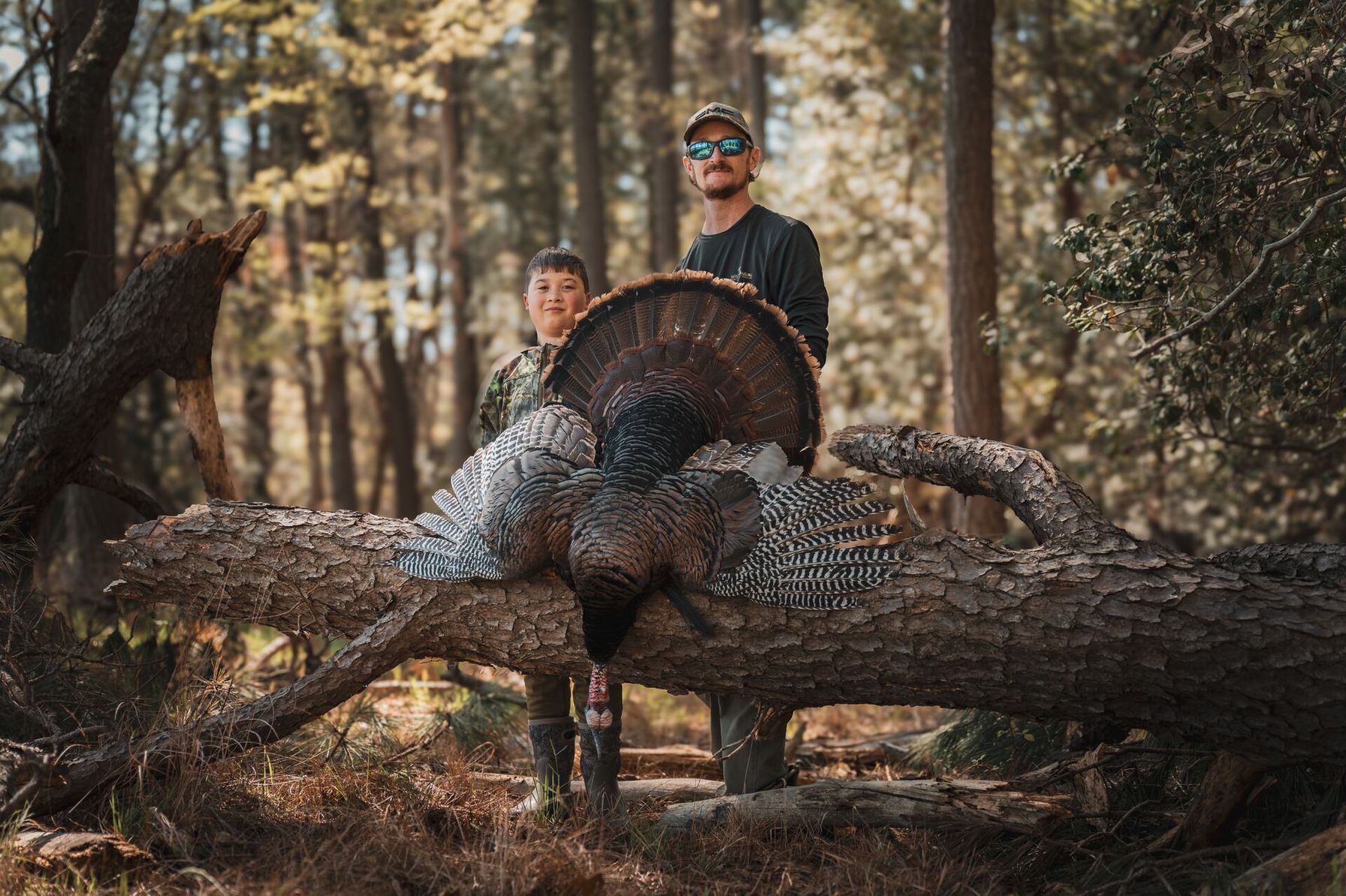 Man and boy smile with turkey after hunt, turkey hunting season success concept.