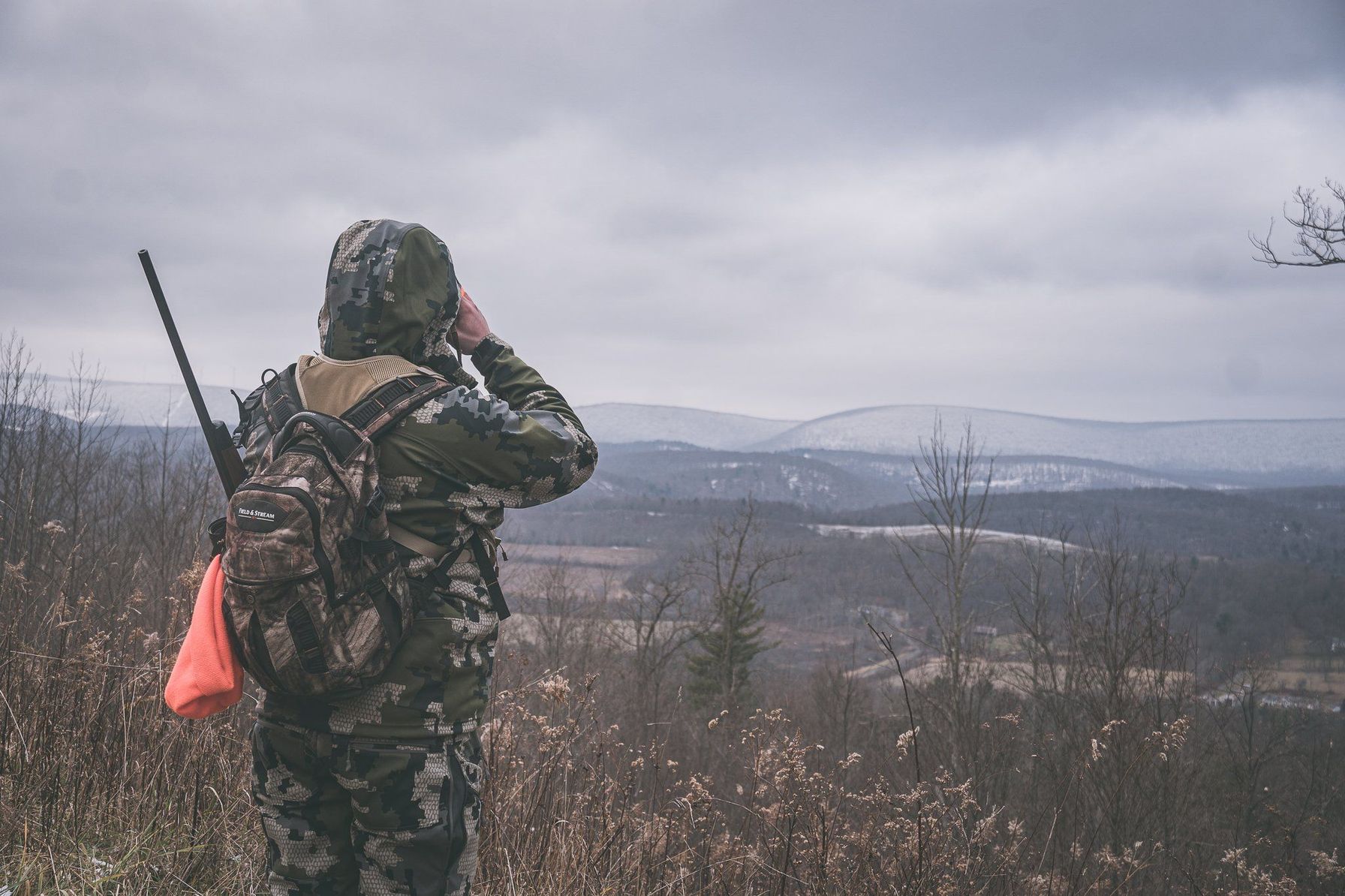 A hunter in camo on a hill using binoculars, prepping for an elk hunt in Wyoming concept.