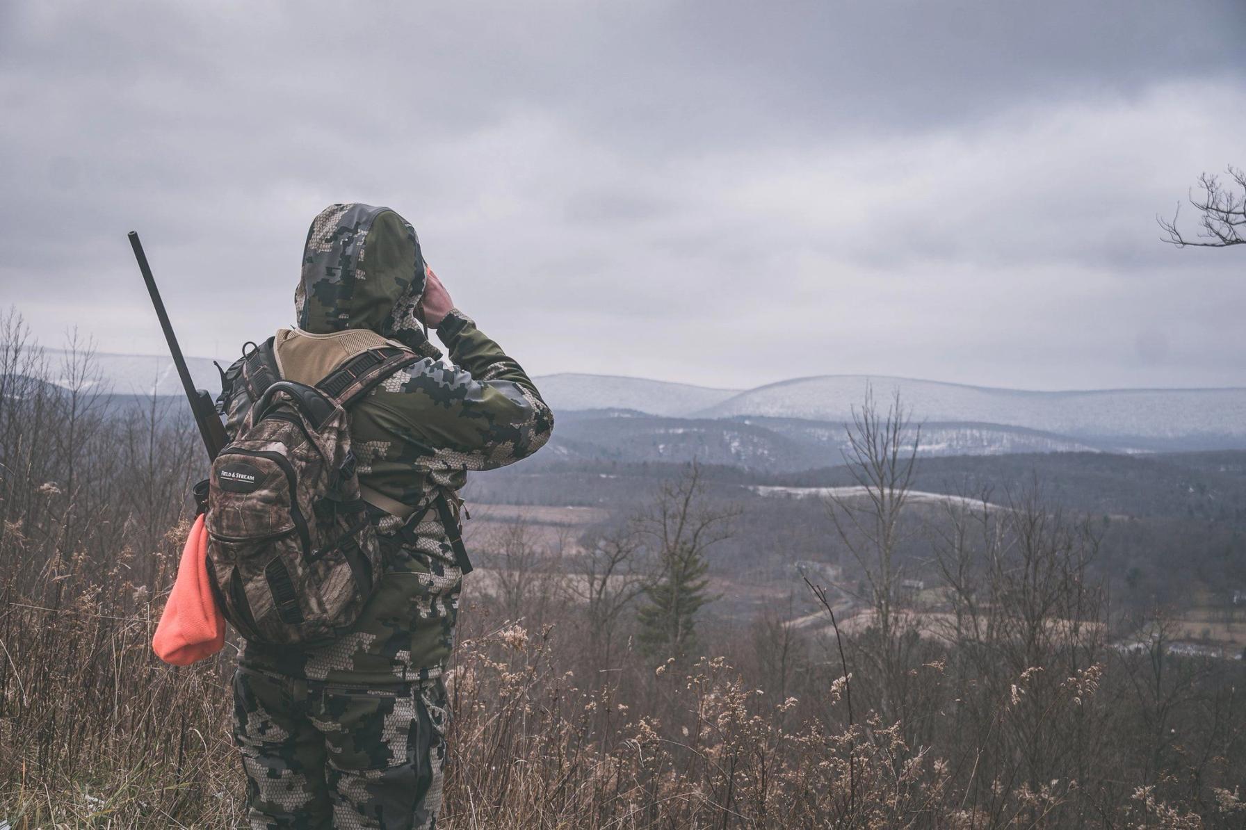 A hunter in camo looking into the distance, spotting black deer concept.