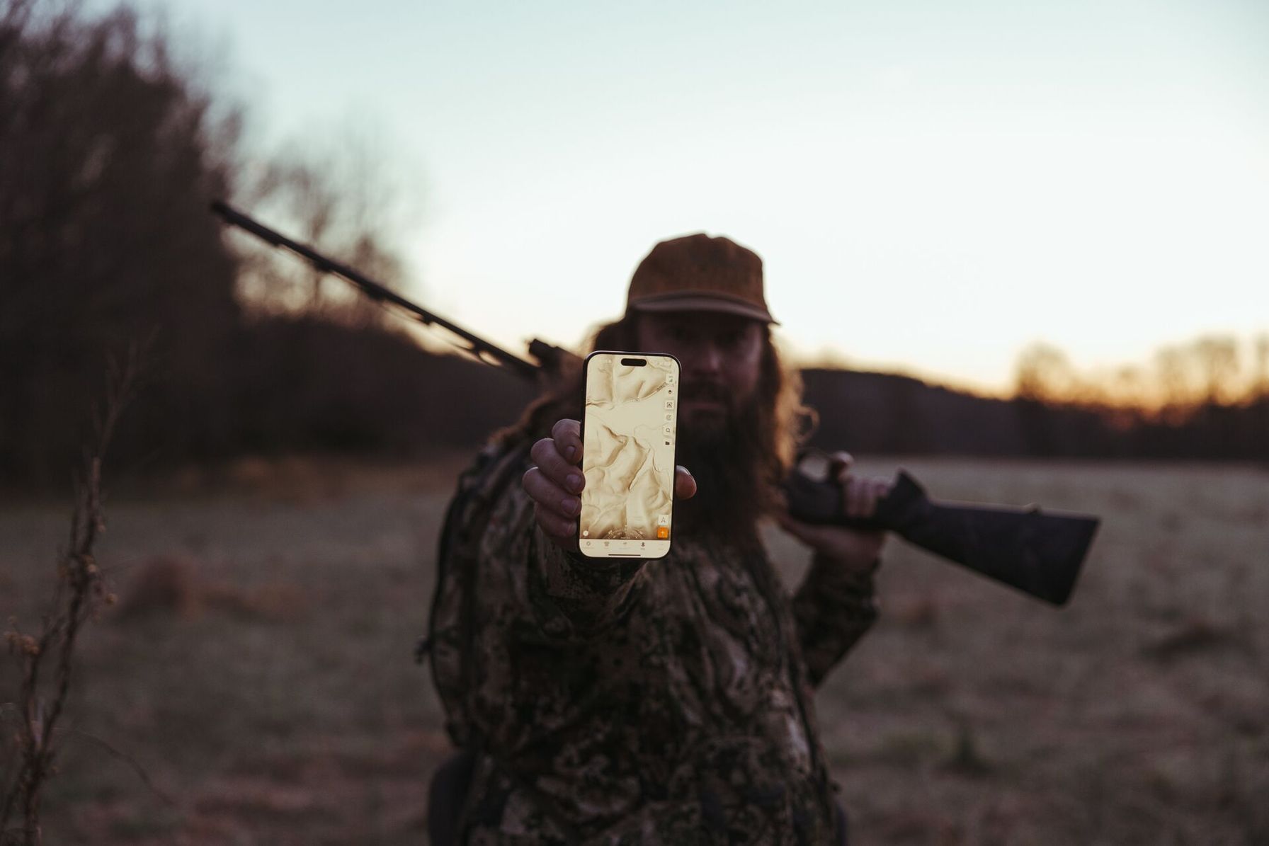 Hunter with firearm holds up a phone showing HuntWise LiDAR map on screen.