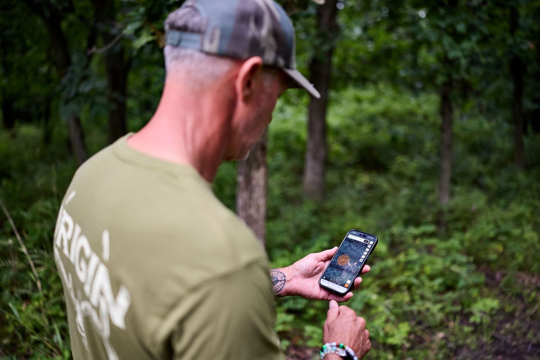 Hunter John Dudley in the woods with a phone showing the HuntWise hunting app.
