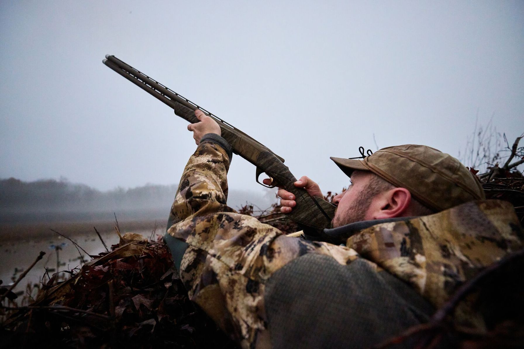Hunter aims shotgun while in duck blind.