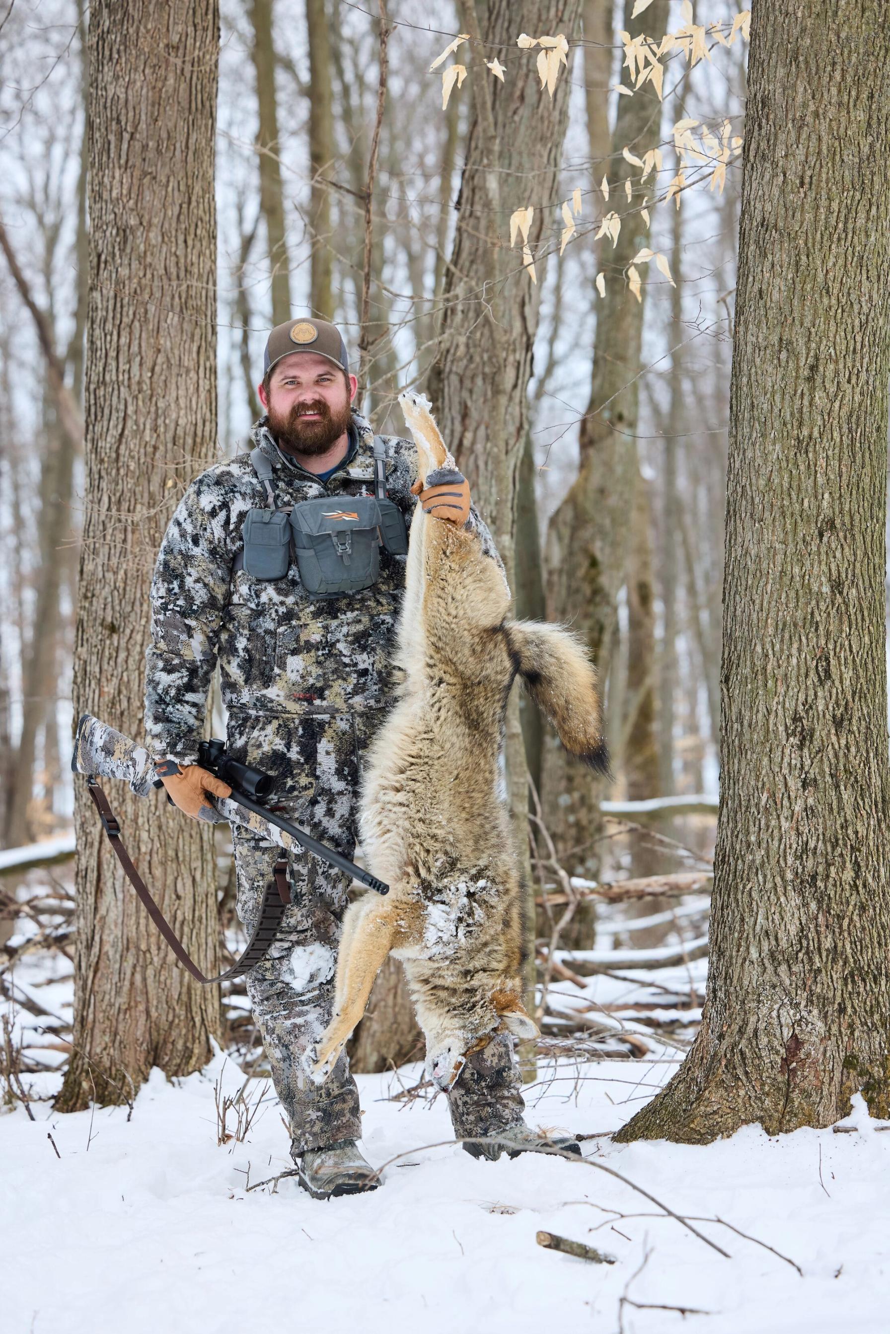 Hunter smiles and holds a coyote up after a hunt, how to hunt coyote concept.