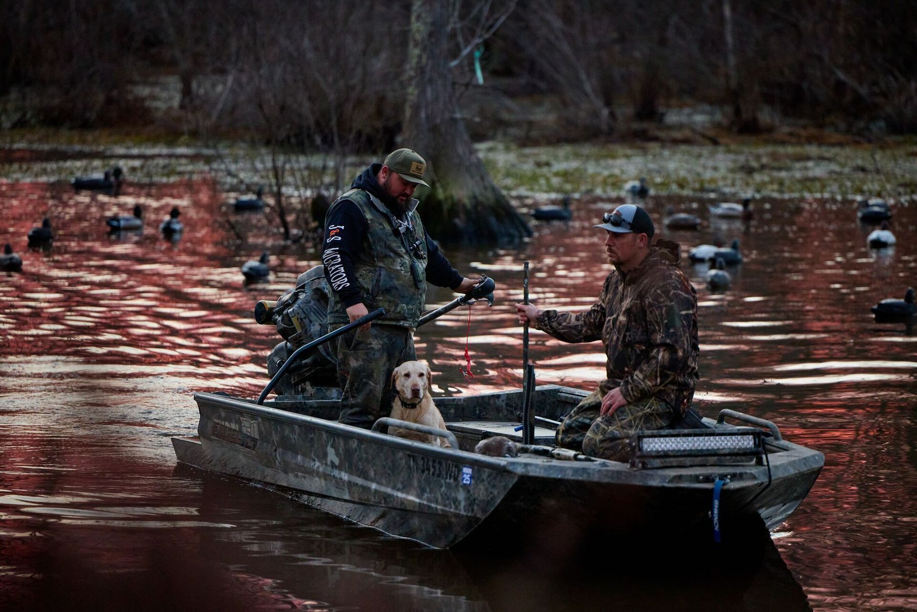 Two hunters in a boat with a dog to hunt waterfowl.