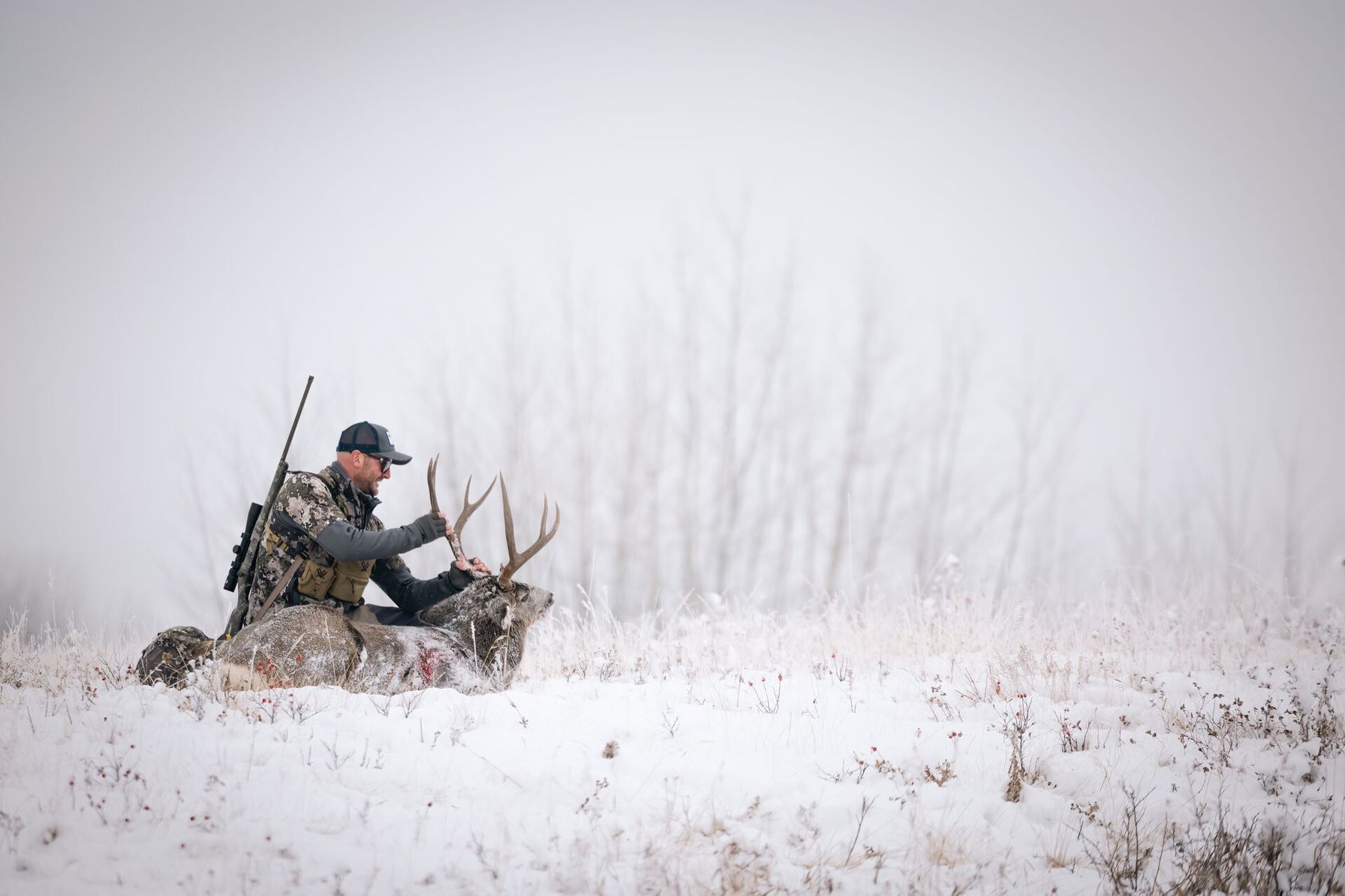 Hunter with rifle and deer on ground in snow, late-season whitetail deer hunting tips concept.