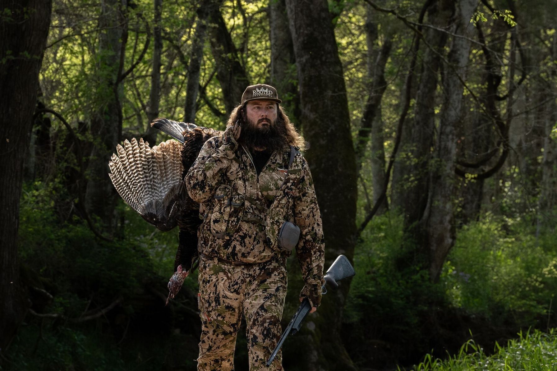 Ben Cole of RootedTV in camo in the woods with a turkey after a hunt.