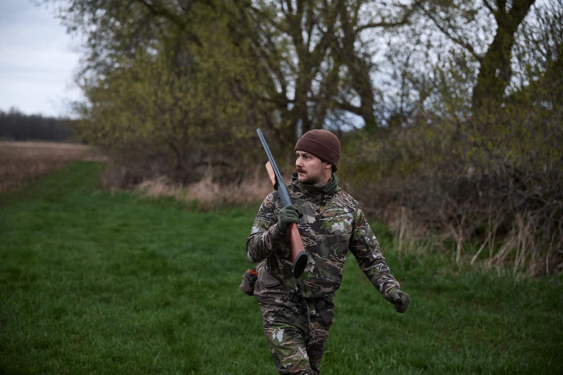A hunter in camo carries a firearm, Ohio hunting concept.