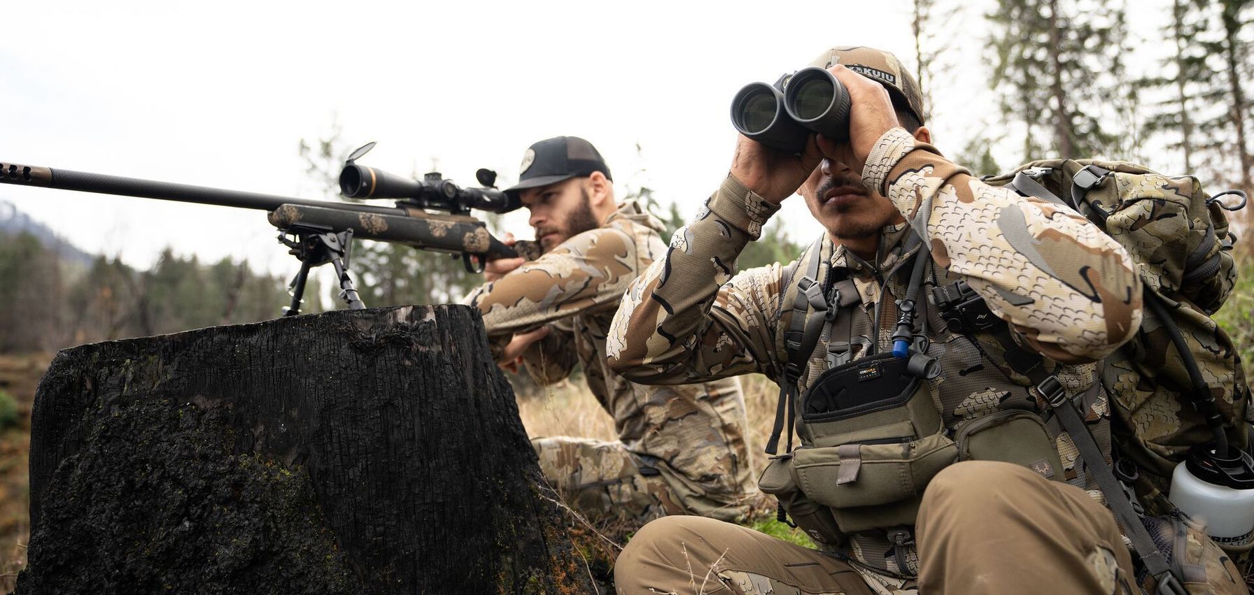 Hunter with rifle and a hunter with binoculars glassing during hunt.