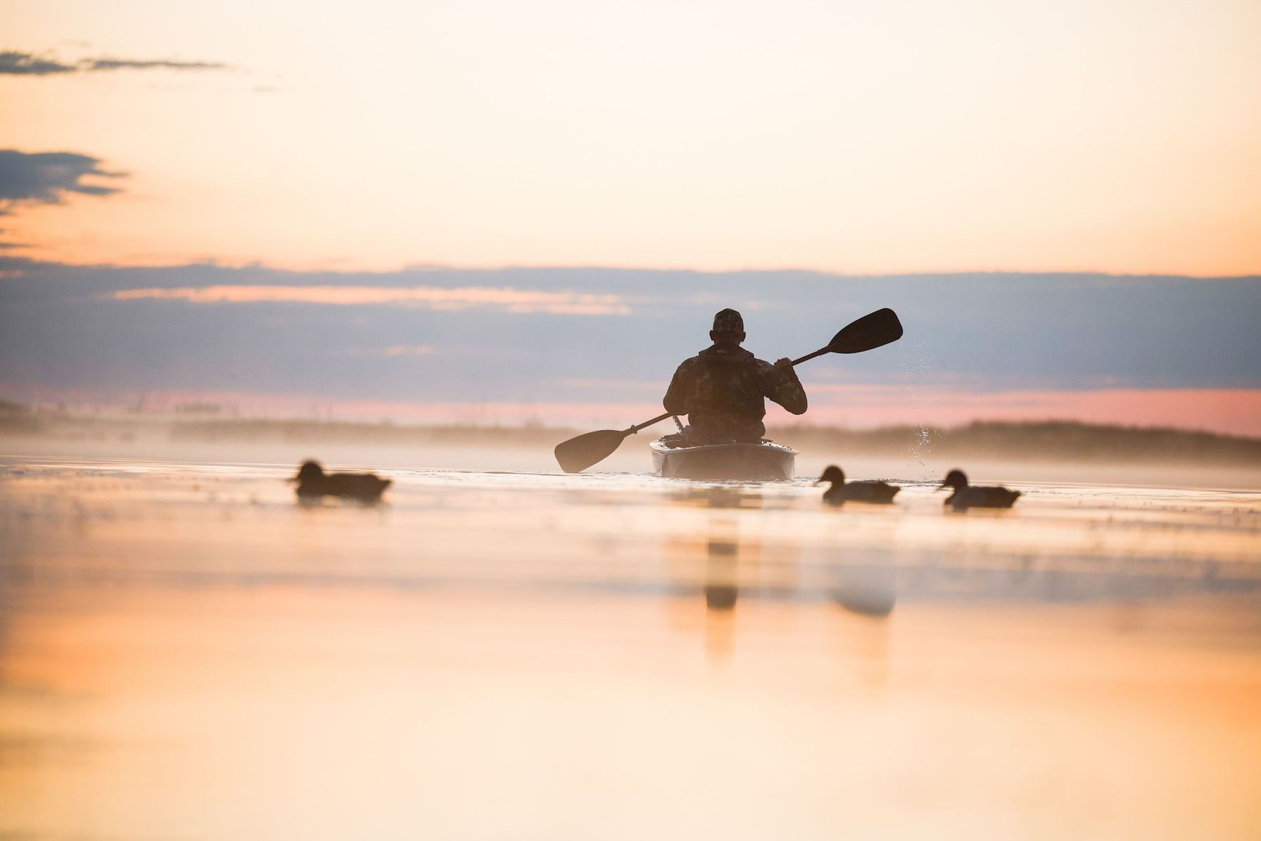 Hunter paddles canoe on water with decoys nearby for a waterfowl hunt.