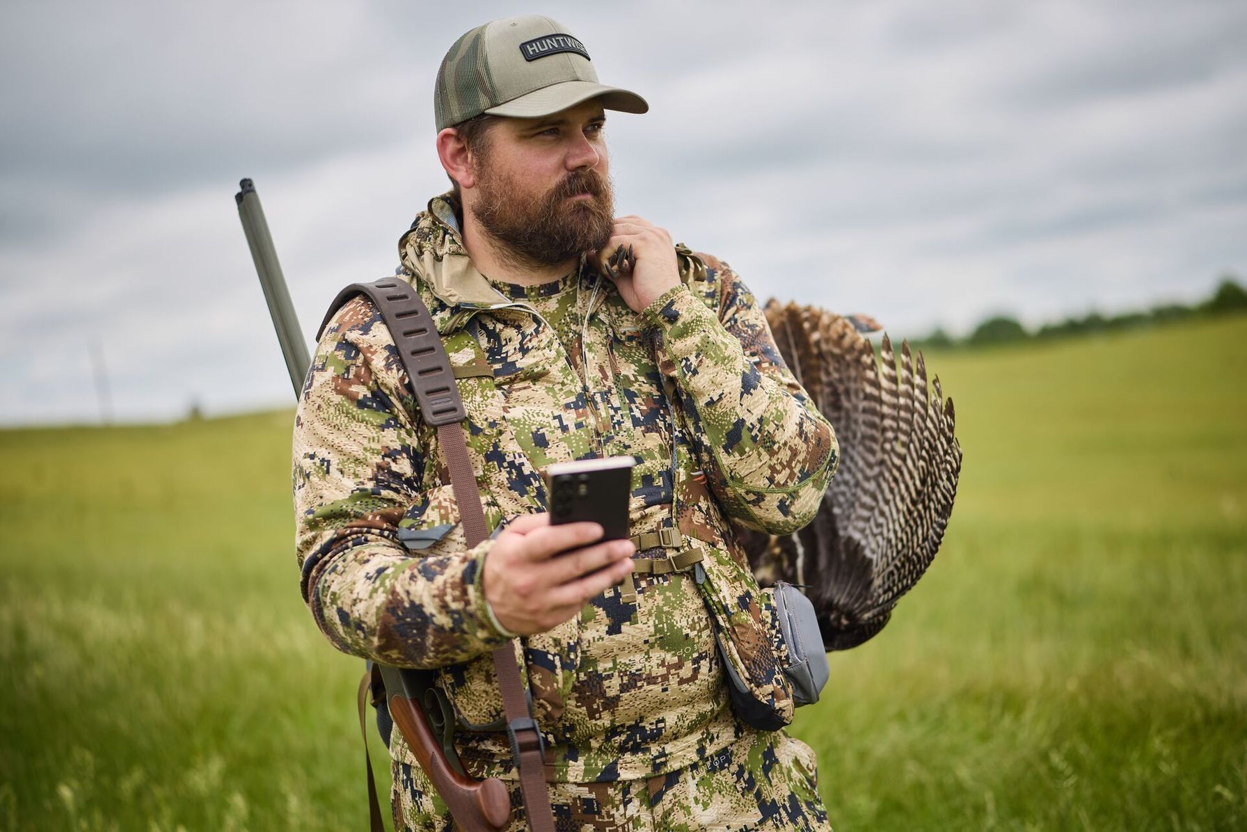 Hunter in camo with turkey gear holding phone, how to use a hunting app to hunt public land.